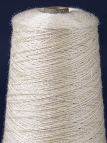Macro photograph of a standardized spindle-wound cone of cream silk yarn, natural side-lit workshop lighting, deep navy background
