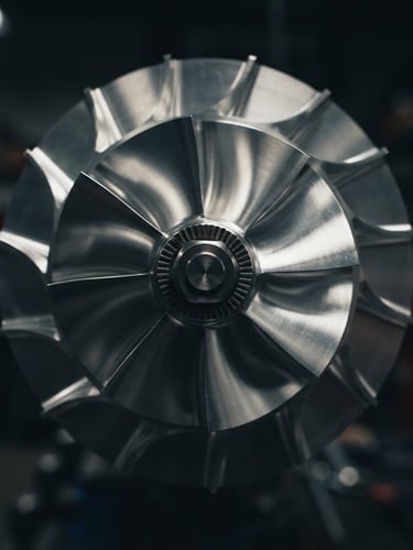 Tight macro shot of a pristine metallic turbocharger compressor wheel, sharp reflections, dramatic workshop lighting, deep charcoal background, 50mm lens