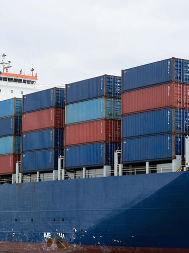 A high-contrast vertical shot of a massive container ship stacked with blue and red cargo containers, overcast daylight, sharp maritime lines.