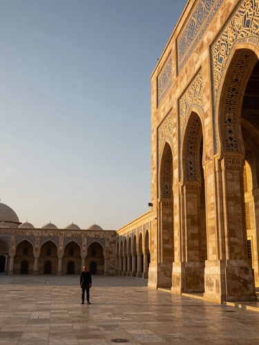 Wide environmental frame, a lone male traveler standing in a grand mosque courtyard at golden hour, ornate stone arches receding into the right third, warm amber light raking across geometric tilework, expansive sky above, figure small against the architecture