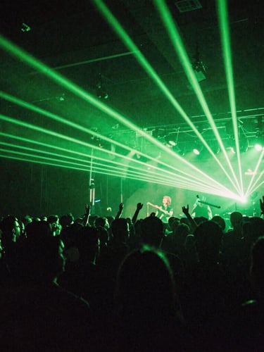 Wide-angle gritty concert crowd shot from behind the stage, intense neon green laser beams cutting through deep shadows, heavy 35mm film grain, electric atmosphere.