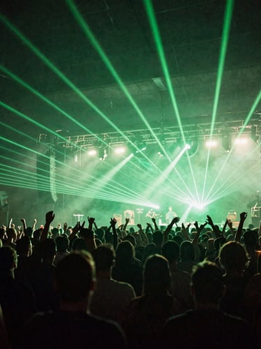 Wide angle shot of a massive concert crowd in Bedford, hands in the air, silhouetted against brilliant green laser lights and heavy stage haze.