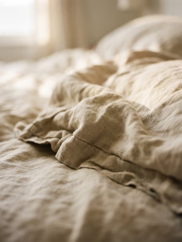 Tight macro shot of soft morning light falling across rumpled oatmeal linen pillow covers, shallow depth of field, 35mm film