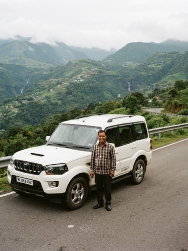 A professional local driver smiling warmly next to a clean SUV parked along a scenic mountain road in Meghalaya, soft overcast daylight, lush green hills in the background, 35mm.
