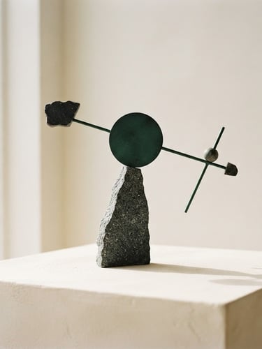 Minimalist geometric balancing sculpture made of textured stone and dark forest green metal, soft architectural shadows, warm ivory background, elegant composition, macro 35mm photography