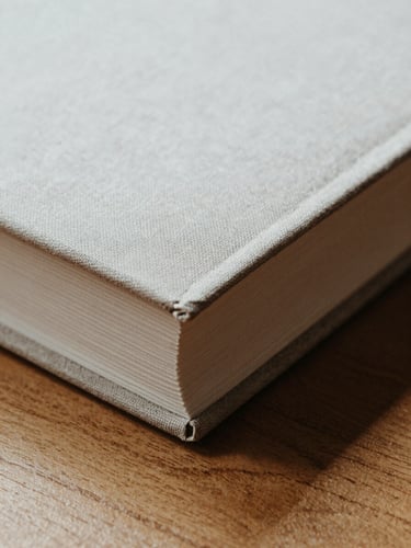 Macro close-up of a heavy linen book cover open on a solid oak table, soft north-facing daylight casting deep shadows