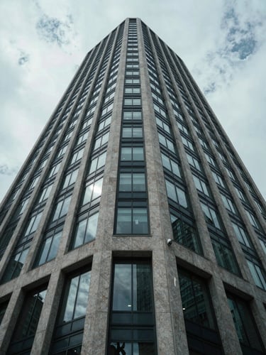 Wide-angle architectural perspective looking up at a modern glass and concrete skyscraper facade under cool, diffused overcast daylight.