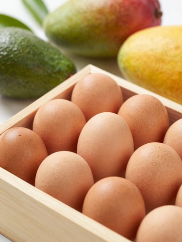 Crisp close-up of fresh brown eggs in a wooden crate, surrounded by exotic fruits like mango and avocado, natural morning light, shallow depth of field, 35mm lens
