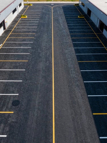 Symmetrical overhead drone shot of a freshly striped multi-acre commercial logistics center parking lot with perfect yellow and white lines, high contrast.