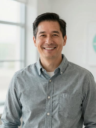 A warm medium environmental portrait of Dr. Andrew Odle, a male physician in his 40s, wearing business casual attire in his bright, modern Liberty Lake clinic, smiling warmly, soft natural window lighting, clean clinical background.