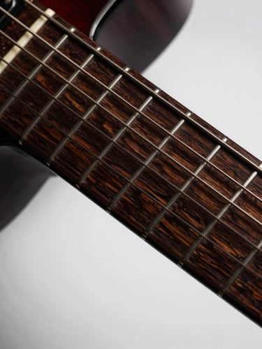 Dramatic close-up of a polished guitar fretboard catching low-key side lighting, rich dark wood grains, high contrast studio photography, 85mm