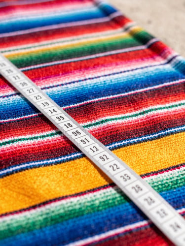 Vibrant pet photography, close-up of a colorful hand-woven Mexican fabric with a tailoring tape measure draped over it, bright natural daylight, shallow depth of field, 35mm