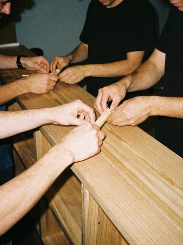 Close-up candid shot of volunteers in a DIY setting, hands building a wooden bar or bookshelf, warm indoor ambient light, raw flash photography feel, 35mm film grain.