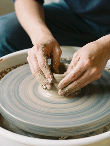 Close-up of hands working with clay on a pottery wheel in a sunlit studio, warm organic tones, authentic craft, 35mm film look