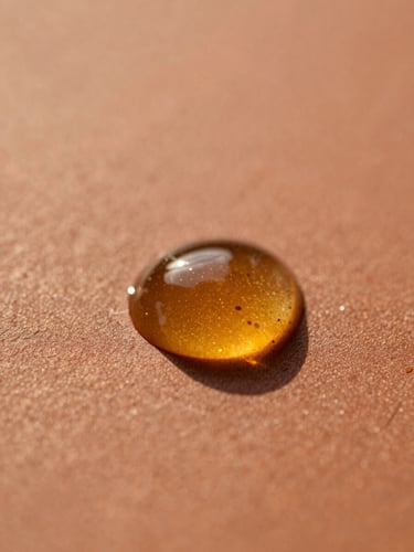 Macro shot of pure amber Argan oil droplets on a warm terracotta surface, golden-hour light