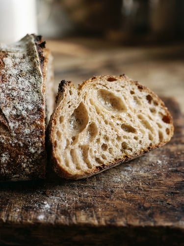 Close-up macro shot of a freshly sliced sourdough boule showing open, wild crumb, flour-dusted crust on a dark wooden surface, soft morning window light, 35mm.