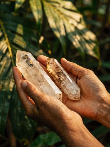 Close-up of hands holding raw quartz crystal over burning copal incense, warm golden hour light filtering through tropical jungle leaves, 35mm