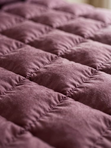 Close-up macro photography of dense plum-toned patchwork quilting stitches under soft natural side-light, highlighting texture and loft, shallow depth of field, 35mm