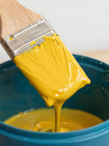 Vibrant editorial photography of a wooden paint paddle dripping rich, thick saffron yellow paint into a deep teal paint bucket, bright high-contrast natural daylight, macro texture of wet paint, shallow depth of field.