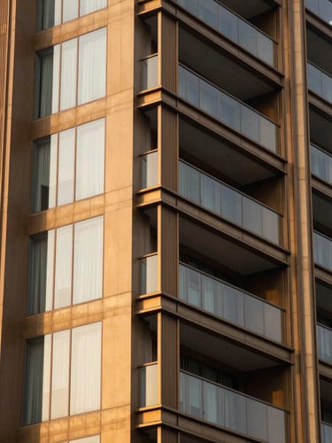 Close-up architectural detail of a modern luxury residential tower facade in Mumbai, warm golden-hour light reflecting off champagne-tinted glass and structural bronze panels, shallow depth of field