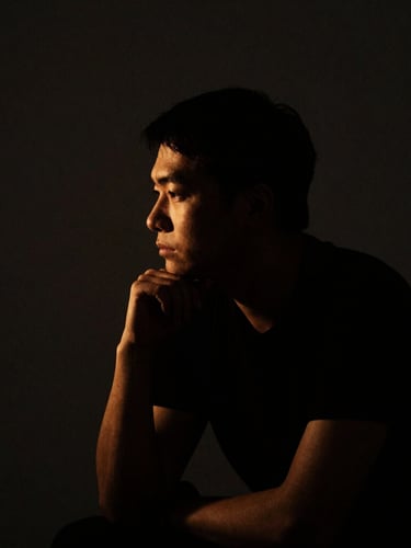 Low-key dramatic portrait of a focused thinker in deep shadow, golden side lighting, minimalist dark background, dark editorial photography, 35mm