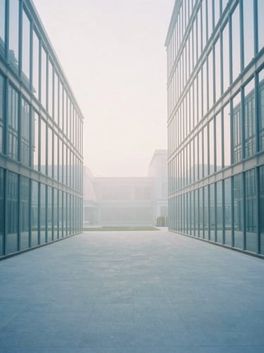 Wide architectural shot of a modern minimalist corporate building with glass facades reflecting soft morning daylight, cool mist blue tones, clean open space, 35mm photography