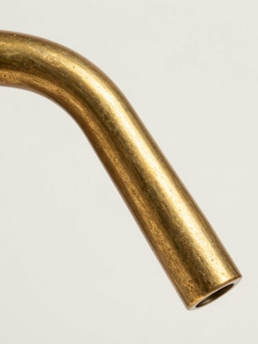 Extreme macro of a brass fixture arm showing hand-applied patina transitioning across the curved surface, studio strobe raking at a low angle to reveal the grain and texture variation, isolated on off-white background, no context objects, clinical framing