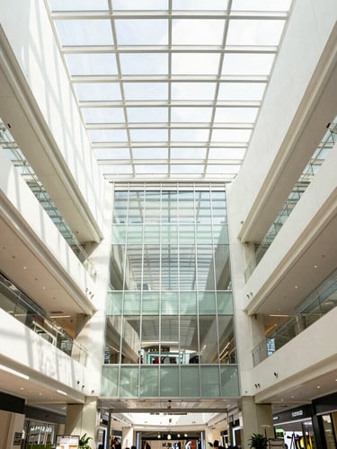 Symmetrical wide-angle architectural photography of a modern commercial mall interior in Kuala Lumpur, bright natural daylight streaming through glass atrium, clean high-contrast corporate tones, sharp details