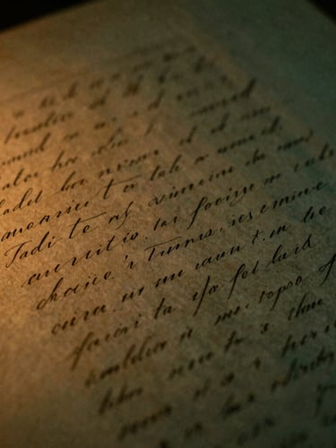 Moody close-up of textured vintage manuscript paper covered in elegant ink handwriting, low-key warm amber side lighting, dramatic shadows, 35mm film grain
