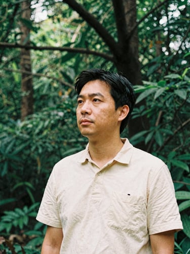 A medium shot of an environmental community leader in warm, natural daylight, looking thoughtfully off-camera, rich forest green tones, medium format film style.