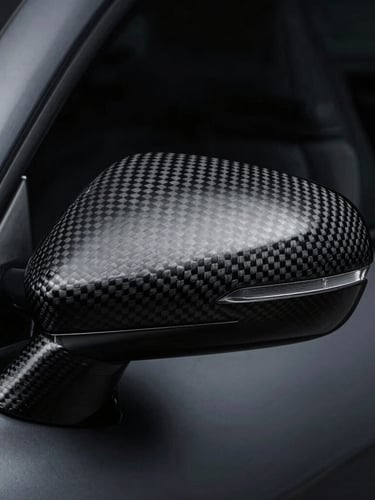 Tight macro shot of a brushed carbon fiber wing mirror, high-contrast studio strobes, moody dark charcoal and metallic tones, sharp details, 35mm lens