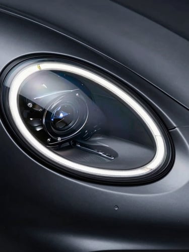 Tight macro shot of a modern sports car headlight reflecting sharp studio LED strips, dark charcoal metallic paint, high-contrast, 35mm lens