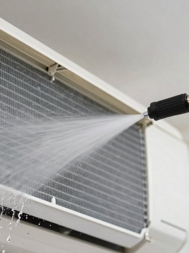 Close-up of a technician's hands in protective gloves using a high-pressure water sprayer to clean the aluminum fins of an indoor AC unit, water droplets visible, clean professional indoor lighting.