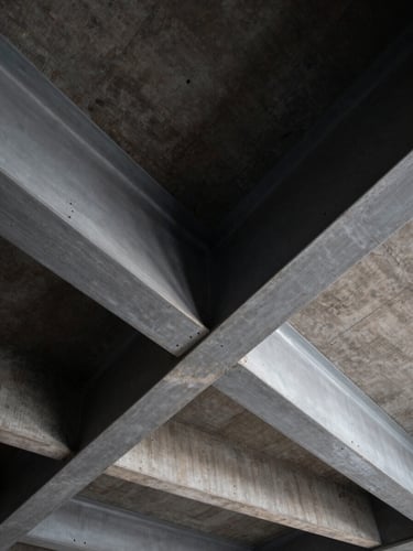 High-contrast architectural close-up of structural steel beams intersecting with reinforced concrete, dramatic shadows, cold steel gray tones