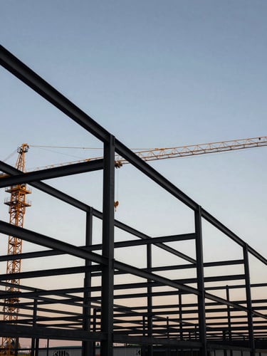 Wide-angle view of heavy steel framing against a high-contrast twilight sky, sharp architectural angles, clean safety-gold accents on cranes, negative space.