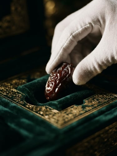 Macro close-up of elegant hands in white gloves meticulously placing a glistening, dark Sukkari date into a velvet-lined, gold-embossed gift box, dramatic side-lighting, deep shadows, rich emerald and gold tones, wide aspect.