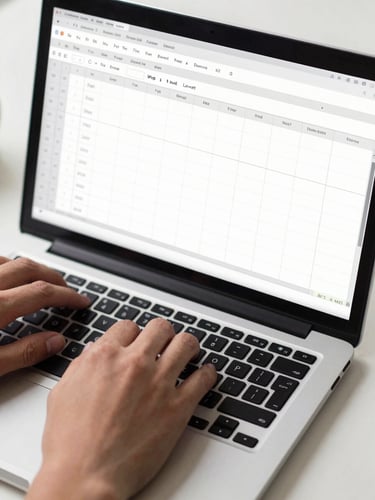 Close-up overhead of hands navigating a Microsoft Excel spreadsheet on a laptop keyboard, crisp studio lighting, clean desk surface visible at edges, no faces, focus entirely on the screen and hands in motion