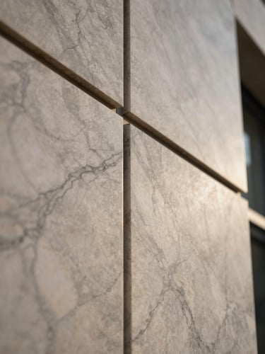 Extreme close-up of ACP panel surface edge-joining a marble-textured cladding panel on a building facade, natural morning sidelight revealing the material depth contrast between flat metal geometry and veined stone texture, no human figures, the joint line running diagonally across the frame