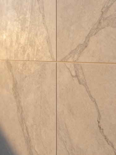 Close-up of a completed marble-texture elevation surface at golden hour, warm raking light revealing the depth of veining and the precision of panel edge joins, no people, full-frame material study