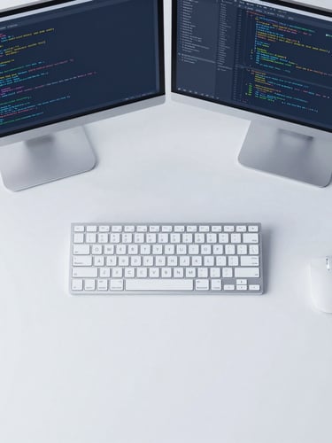 Clean top-down flat lay of modern tech gear, dual monitors displaying code and data flow, crisp cool daylight, minimalist tech photography