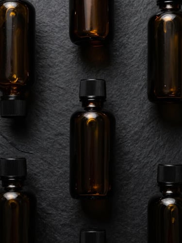 Top-down flat lay of minimalist dark glass bottles on a black slate surface, soft golden side lighting, premium packaging
