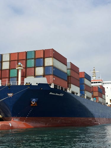 Low-angle heroic shot of a massive industrial container vessel docked at a Nigerian deepwater port under an overcast maritime sky, sharp architectural shadows, high-contrast natural light.