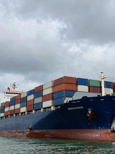 Low-angle heroic shot of a massive container ship docked at a busy Nigerian port under a dramatic, overcast maritime sky.