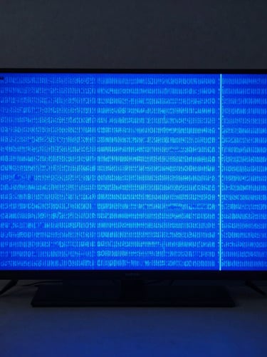 Straight-on shot of a modern television screen displaying a vibrant blue diagnostic test pattern in a clean, high-tech workshop environment.
