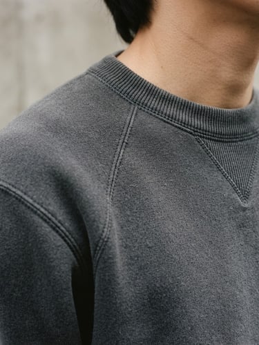 A close-up vertical shot of a charcoal gray heavyweight cotton sweatshirt, focusing on the thick ribbed collar and clean shoulder seams, soft overcast daylight, desaturated neutral tones, 35mm film grain