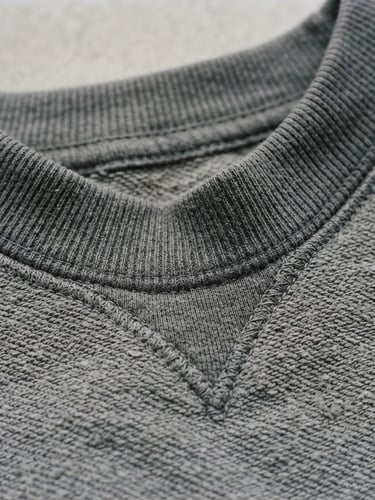 Close-up of a heavy structured grey cotton sweatshirt collar, showing thick double-needle stitching, natural overcast daylight, matte finish