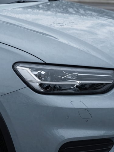 Close-up detail of a modern vehicle headlight and fender, overcast New England daylight, cool slate gray tones, sharp architectural framing
