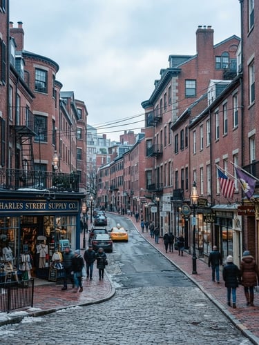 Wide-angle editorial photograph of historic Charles Street brick architecture in Boston, overcast New England daylight, cool blue and slate tones, 35mm