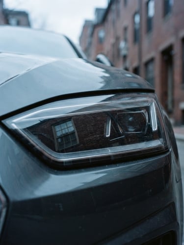 Crisp editorial photography of a modern vehicle headlight reflecting historic Boston brickwork, overcast New England daylight, cool blue and slate tones, 35mm.