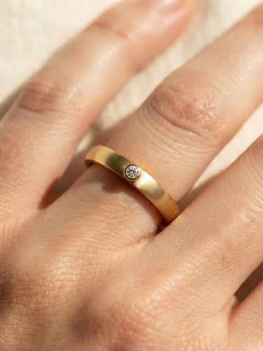 Extreme close-up of a tarnish-resistant gold ring on a hand, warm cream background, direct sunlight casting sharp elegant shadows, macro lens, 35mm
